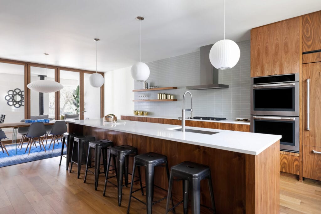 Cuisine moderne avec tabourets de bar en métal noir et îlot en bois avec comptoirs blancs.