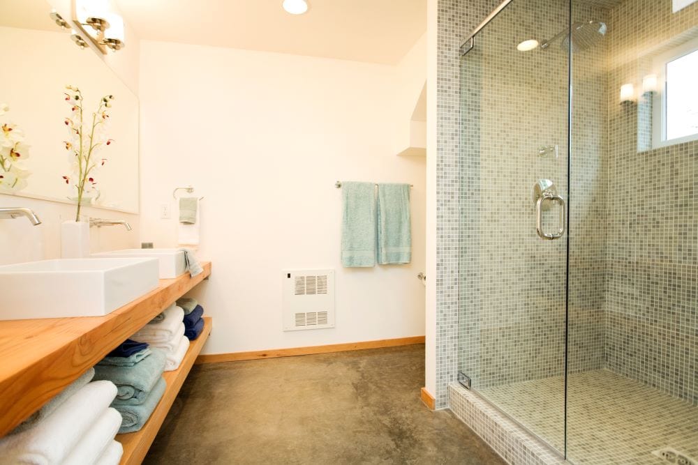 Salle de bain avec des accents verts dans les serviettes et le carrelage de la douche.